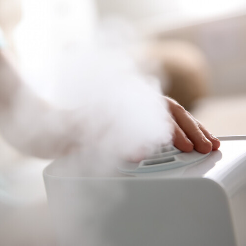 Woman using modern air humidifier at home, closeup